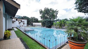 A swimming pool with a surrounding fence, a grassy area, and a building with a sloped roof. - Lembah Gunung Kujang by ARBA (Cijambe)
