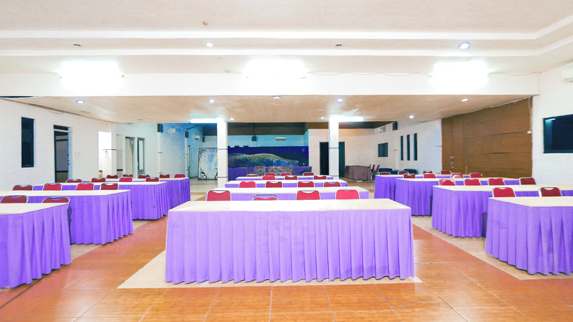 Une salle de conférence avec plusieurs tables recouvertes de nappes violettes, disposées en rangées.