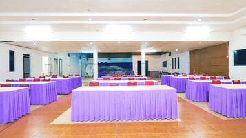Uma sala de conferência com várias mesas cobertas por toalhas roxas, dispostas em fileiras.