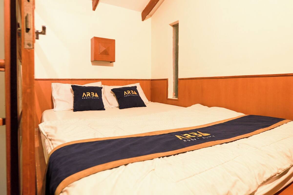 Een hotelkamer met een bed, twee kussens met 'ARBA HOSPITALITY'-branding, een houten hoofdeinde en een raam met uitzicht.