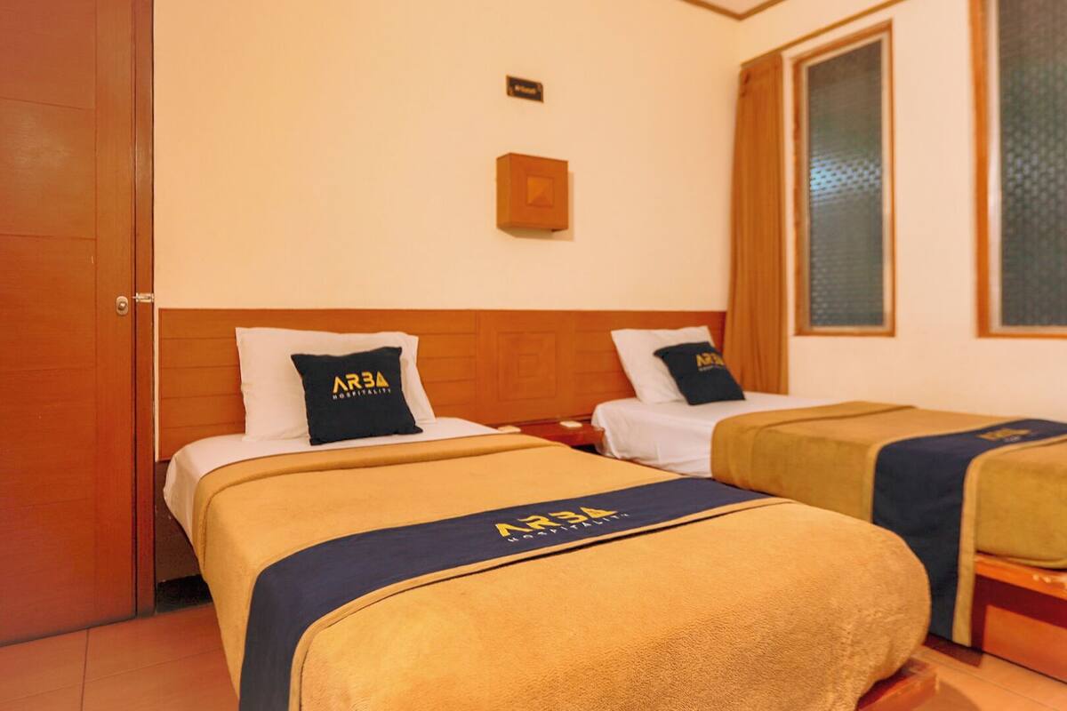 Een hotelkamer met twee bedden, elk voorzien van een hoofdeinde en een kussen met het AR34 Hospitality logo.