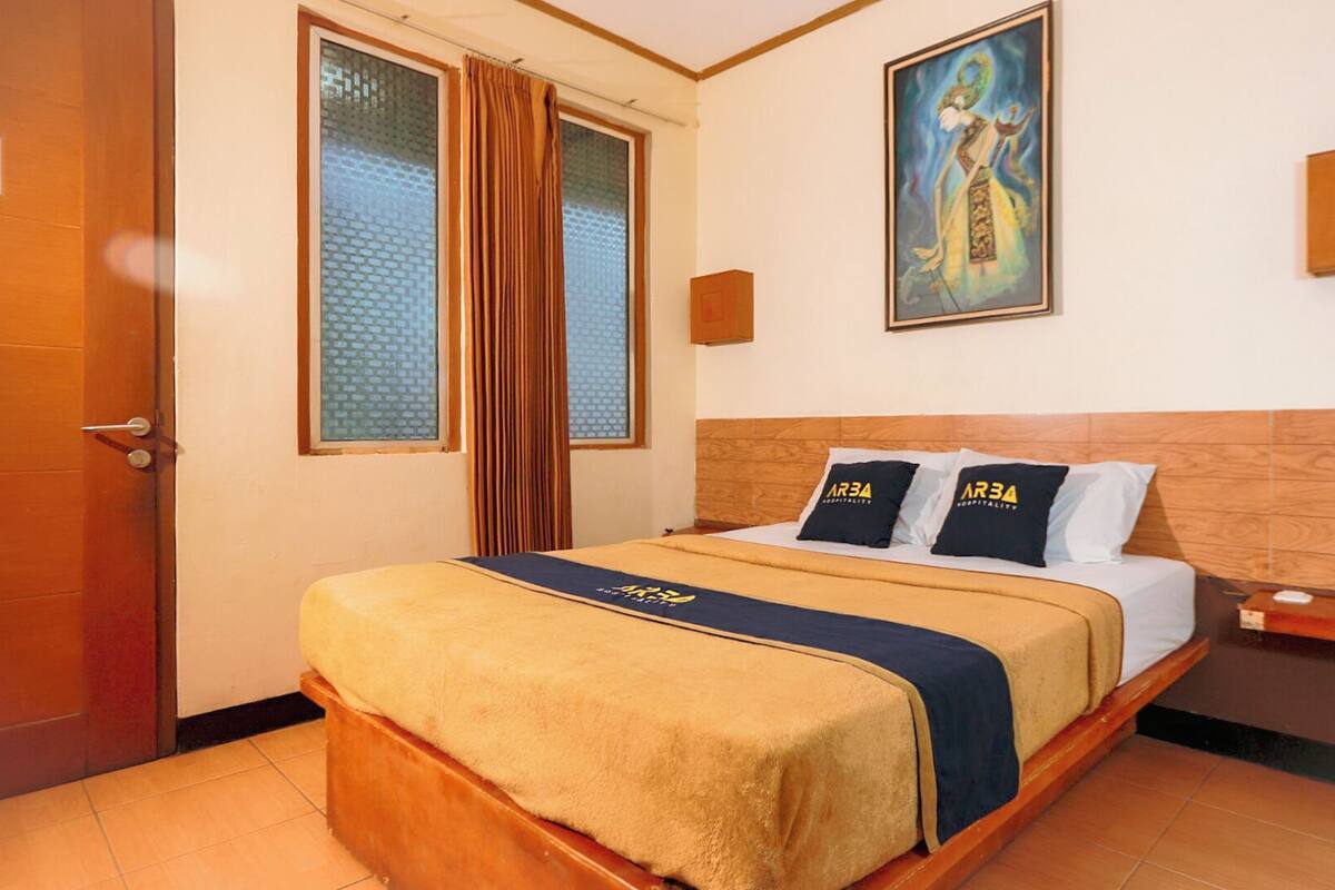 Een hotelkamer met een bed, een schilderij aan de muur en een deur met een bordje.