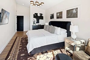 Un dormitorio moderno con una cama grande, una mesita de noche con lámpara, una silla y obras de arte en las paredes.