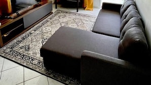 Un salon moderne avec un canapé d’angle, un téléviseur à écran plat, une table basse et un tapis à motifs.