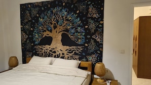 Une chambre à coucher avec un lit, une tapisserie ornée d’un motif d’arbre et deux lampes sur une table de chevet.