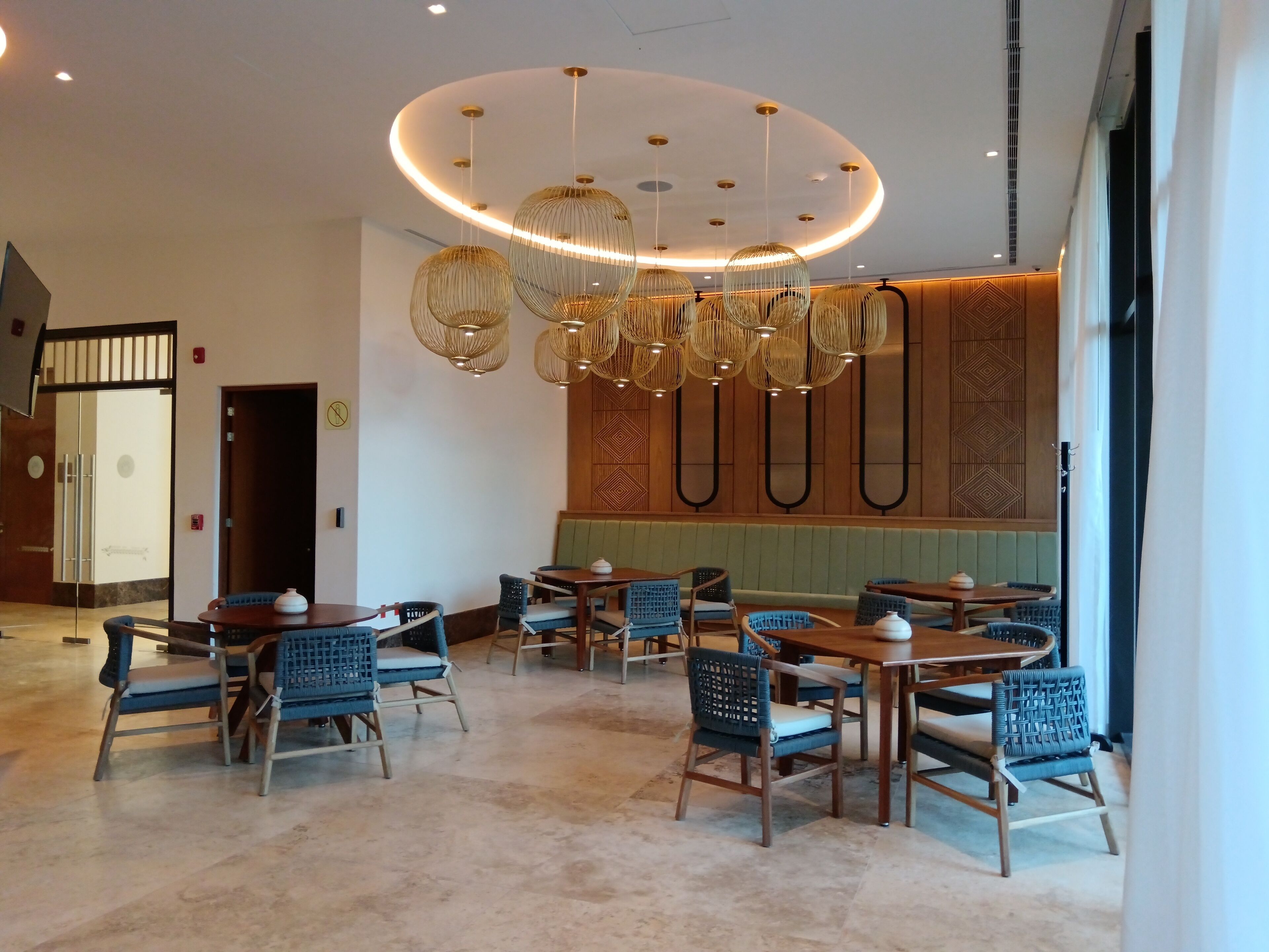 A modern restaurant interior with round tables, blue chairs, and a unique ceiling light fixture.