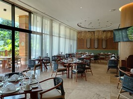 Un restaurante con varias mesas dispuestas con vajilla blanca, sillas de mimbre y un amplio ventanal con vistas a la vegetación.