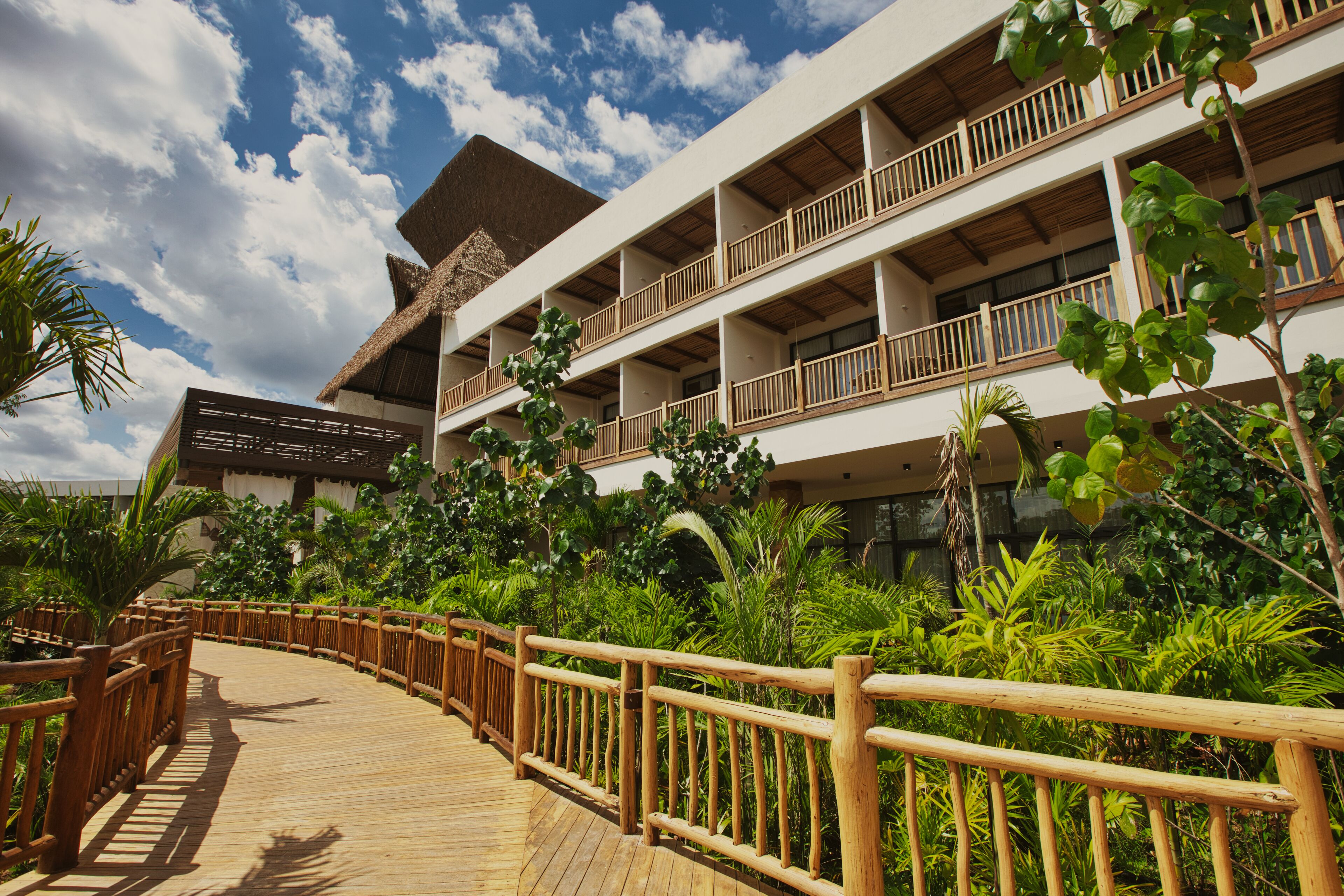 A resort with a wooden boardwalk, lush greenery, and multi-story buildings with balconies.