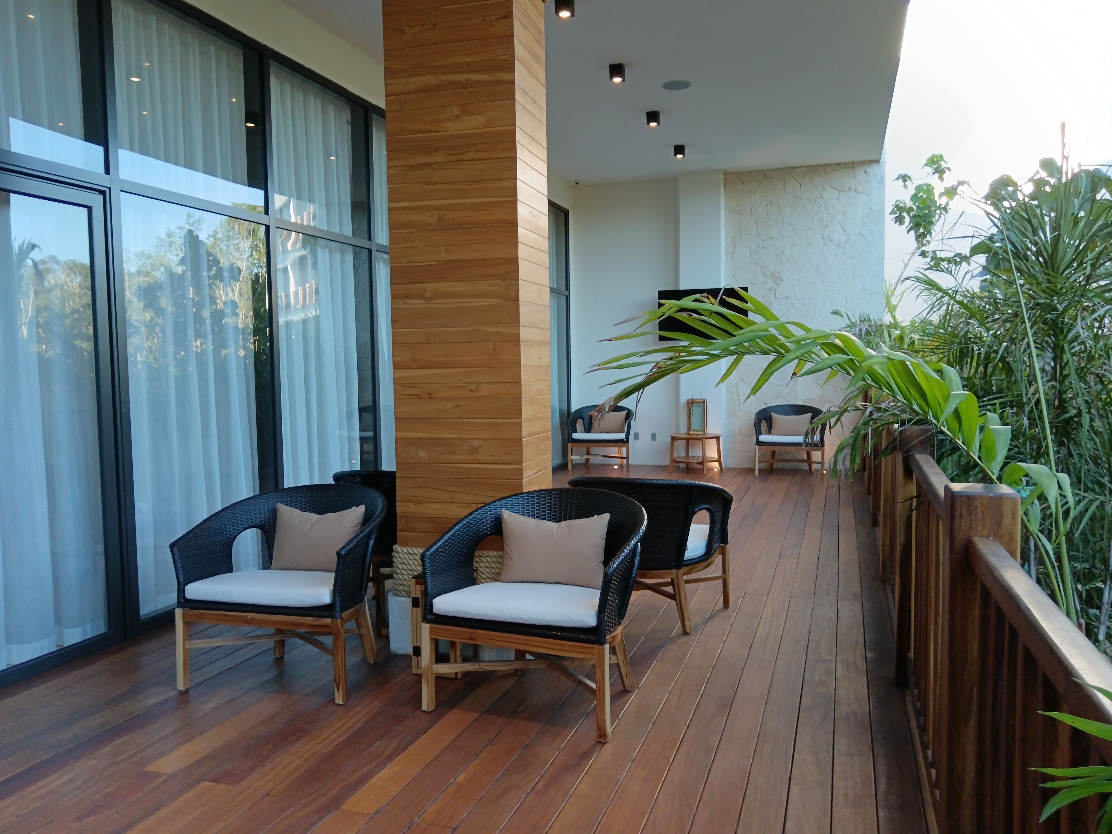 A spacious balcony with wicker furniture and a wooden floor, overlooking a garden.