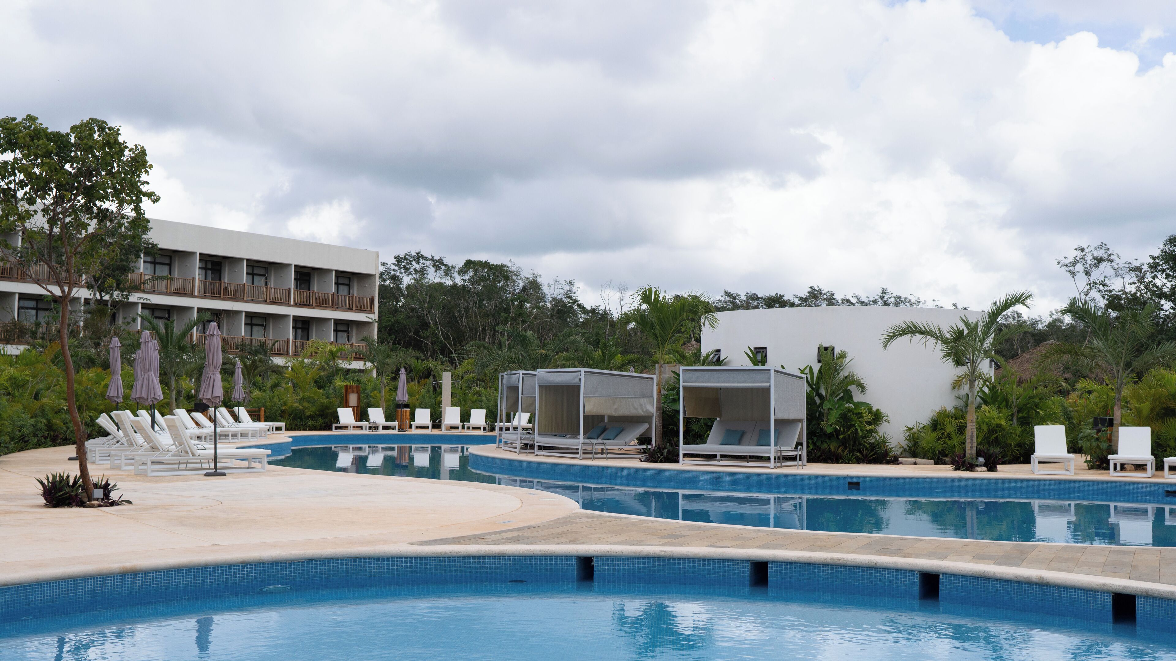 Zona de piscina en un resort, con varias piscinas, tumbonas y sombrillas.