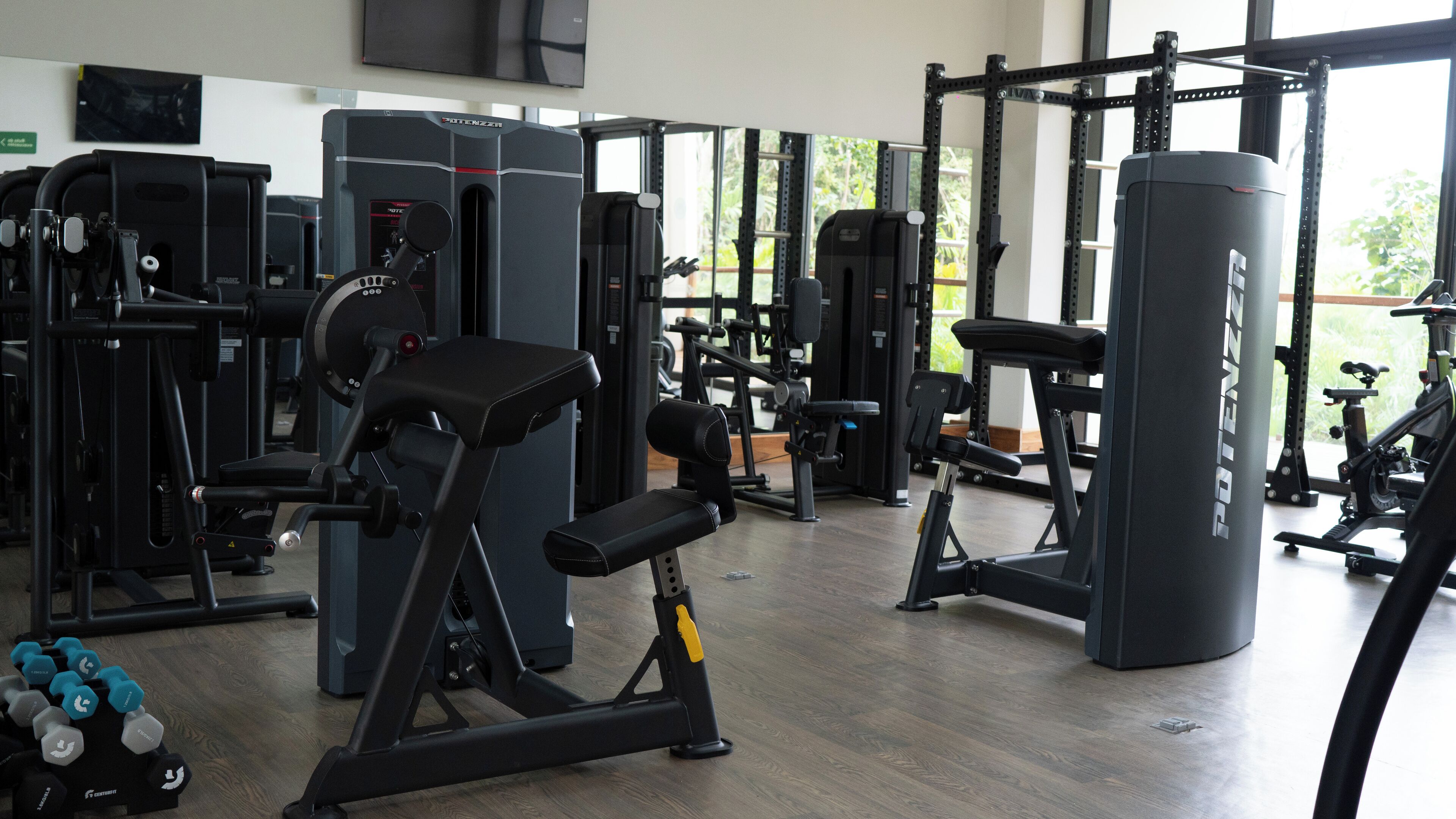 Een sportschool met diverse fitnessapparaten, waaronder krachttoestellen, losse gewichten en een bankdrukpers.