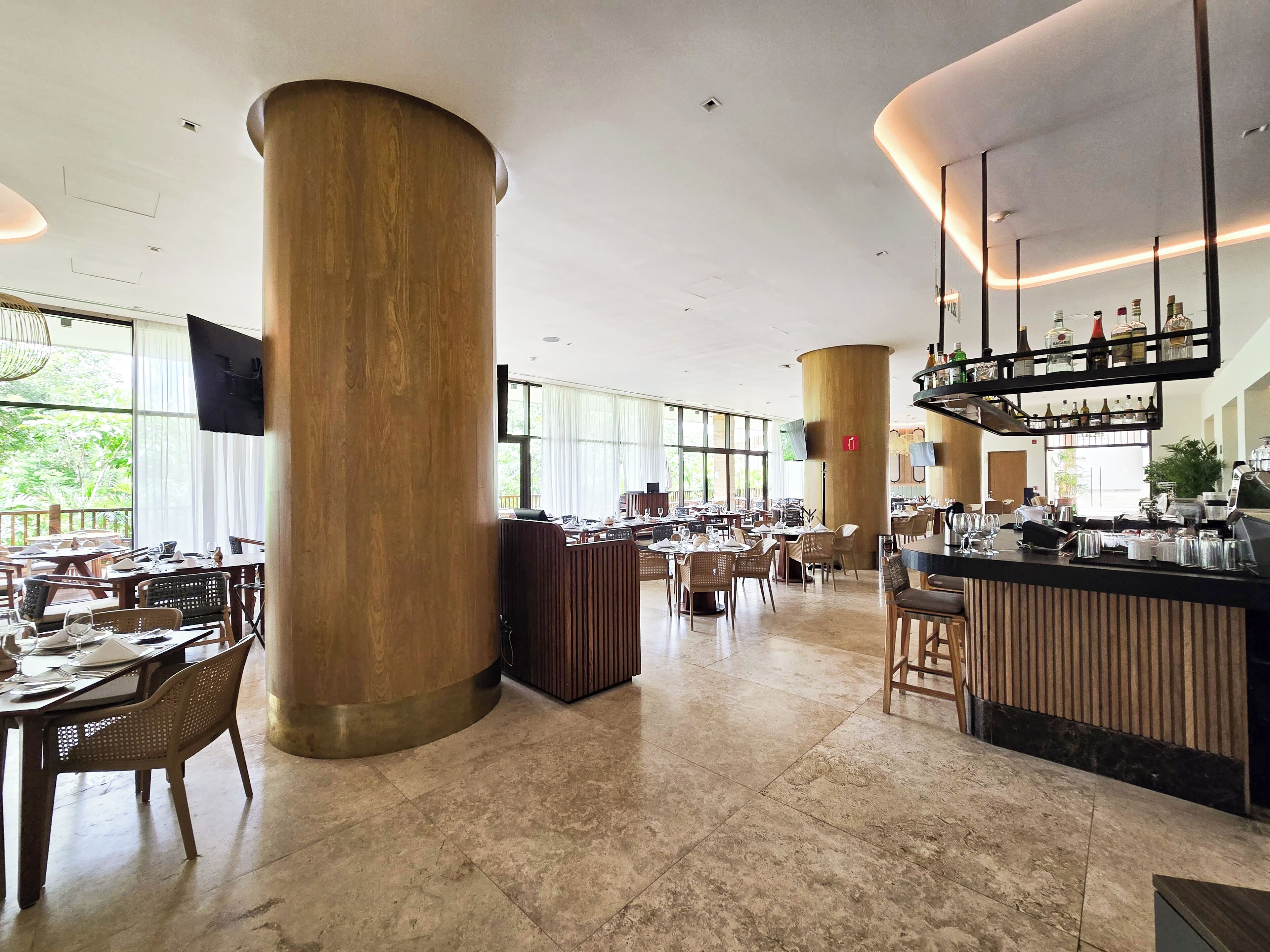 A spacious restaurant with high ceilings, large wooden pillars, and a bar area with a variety of bottles.