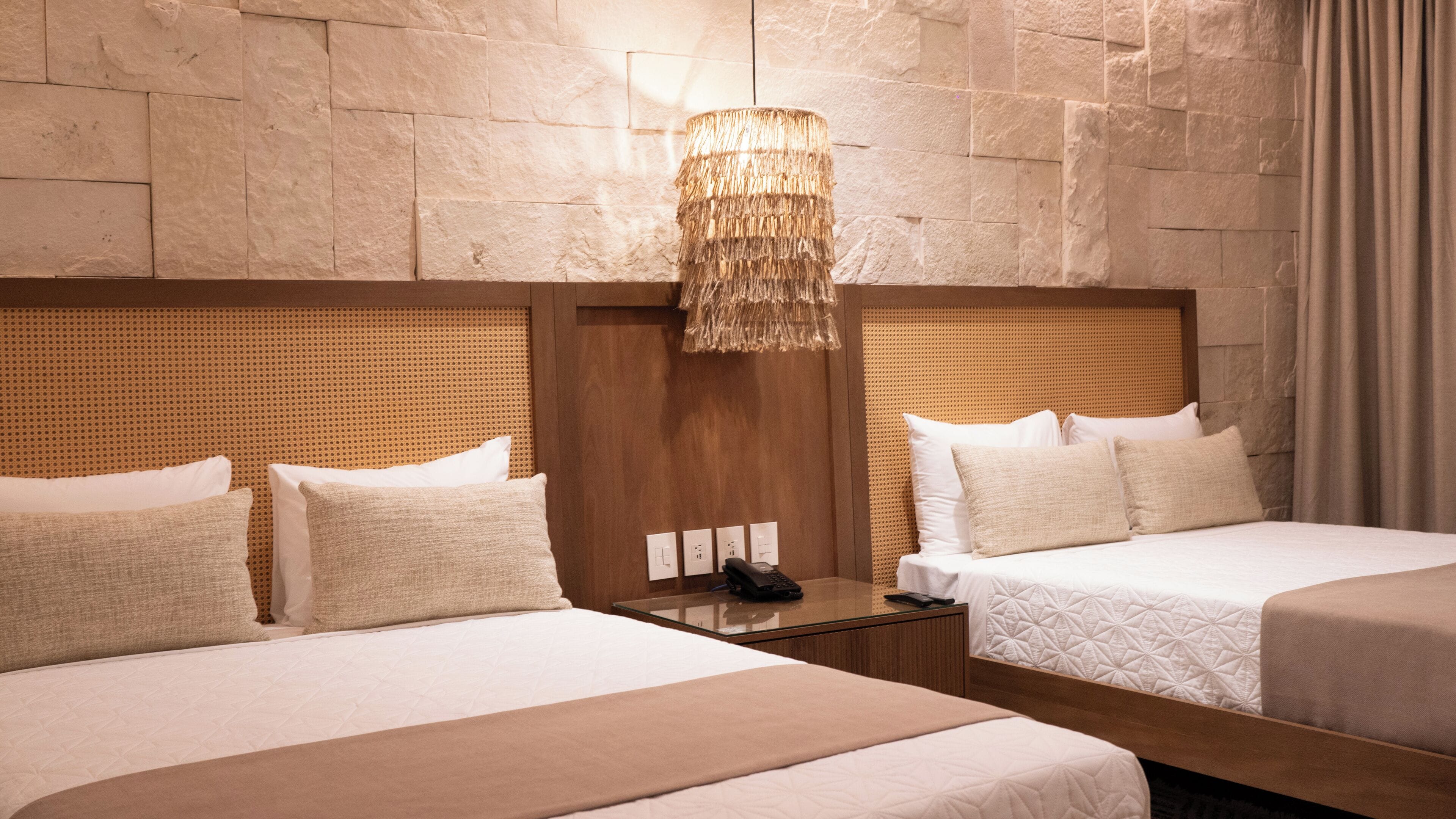 Ein Hotelzimmer mit zwei Betten, einem Holzkopfteil, einer strukturierten Wand und einer Hängelampe.