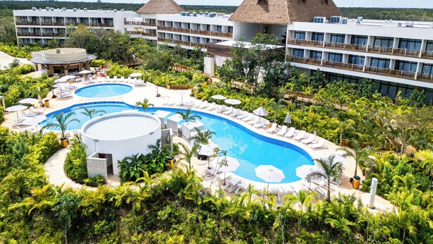 Ein Resort mit einem großen Schwimmbad, mehreren Gebäuden mit Balkonen und üppiger Vegetation.