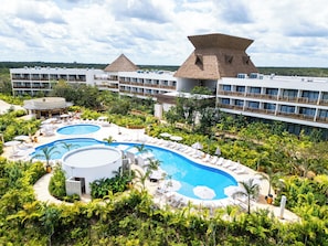 Un resort con una amplia piscina, varias edificaciones con balcones y exuberante vegetación.