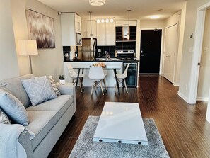 A modern living room with a grey sofa, a coffee table, and a dining area with white chairs.