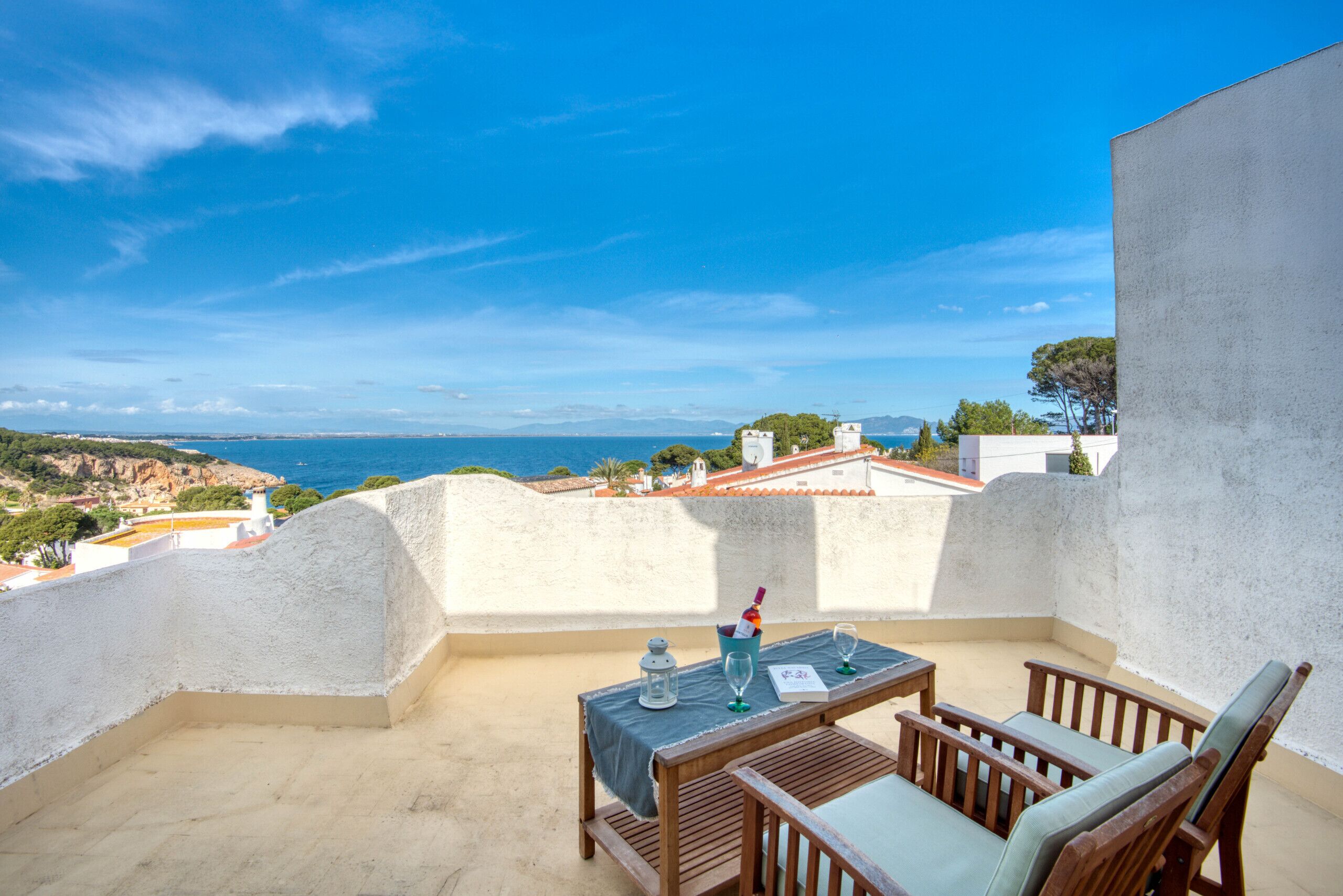 A terrace with a table and chairs, overlooking a coastal landscape.