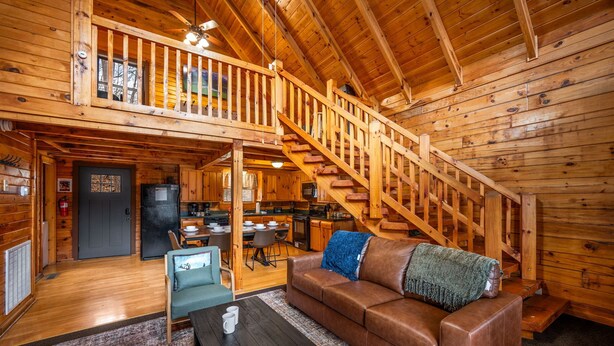 A wooden cabin interior with a dining area, kitchen, and a staircase. - Cozy Cabin Retreat: Hot Tub, Fire Pit & Game Room – Perfect Getaway! (Sevierville)
