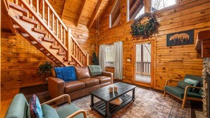 A wooden cabin interior with a staircase, leather sofa, coffee table, and a fireplace. - Cozy Cabin Retreat: Hot Tub, Fire Pit & Game Room – Perfect Getaway! (Sevierville)