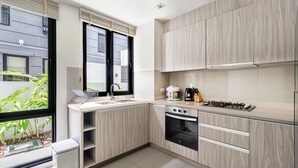 Een moderne keuken met lichte houten kastjes, een ingebouwde oven, een gasfornuis en een raam met zonwering.