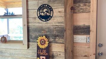 A rustic cabin interior with a wooden wall, a circular emblem, and a vertical sign with the word 'Hello' and sunflowers.