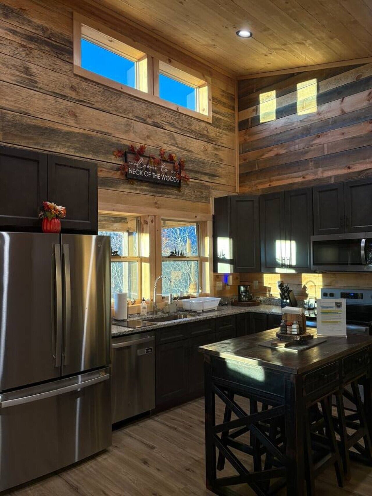 A kitchen with wooden walls, a stainless steel refrigerator, a sink, and a bar area.