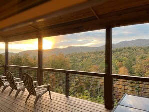 Une terrasse en bois avec des chaises, donnant sur un paysage boisé au coucher du soleil.