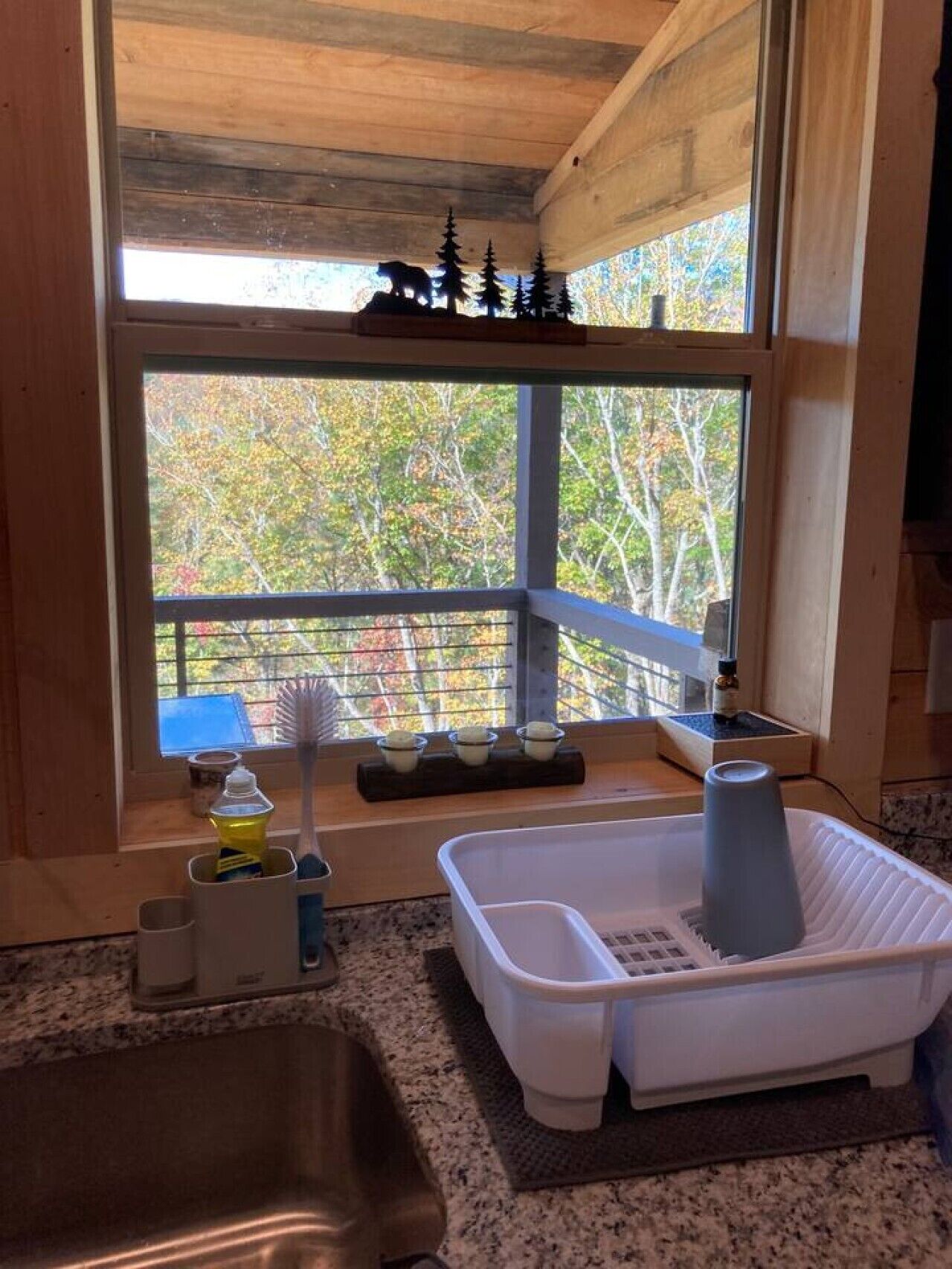 Eine Küche mit einem großen Fenster, einem Spülbecken, einem Wäscheständer und einem kleinen Regal mit Gegenständen.