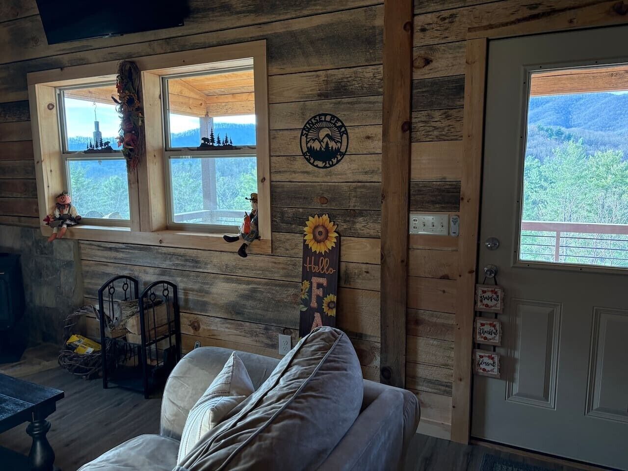 Interior acogedor de una cabaña con exterior de madera, un sofá, una jaula de pájaros y una puerta que ofrece vistas al exterior.