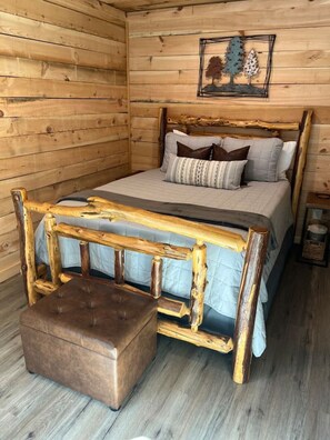 Une pièce de style cabane en bois, avec un lit, un banc et un tableau accroché au mur.
