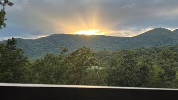 A view of a forested mountain range with a sun setting behind the hills.