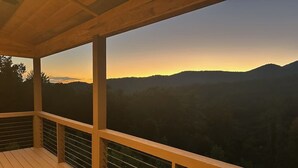Une terrasse en bois offrant une vue sur un paysage montagneux au coucher du soleil.