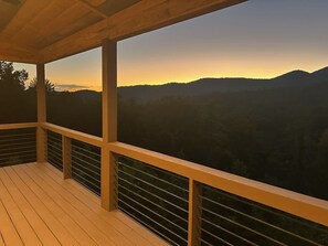 Eine Holzterrasse mit Blick auf eine gebirgige Landschaft im Sonnenuntergang.