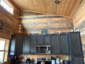Une cuisine avec des murs en bois, des meubles de couleur sombre, un four à micro-ondes, une cuisinière et une fenêtre.