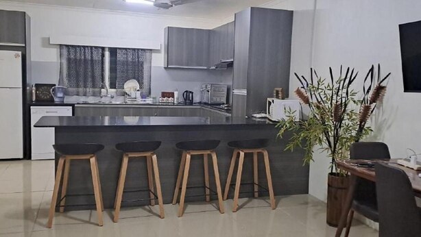 Une cuisine moderne dotée d’un îlot central, de tabourets de bar, d’une table à manger et d’une plante en pot.