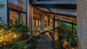 A modern building with a wooden deck, glass railings, and tropical plants. - Villa Baratega (Kerobokan)