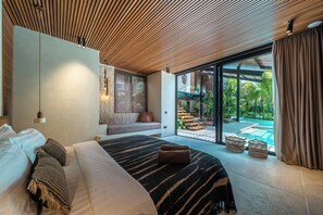 A modern bedroom with a large bed, a seating area, and a view of a swimming pool. - Villa Baratega (Kerobokan)