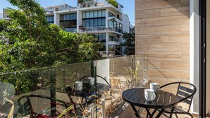 Ein moderner Balkon mit Glasgeländer, einem runden Tisch mit Stühlen und Blick auf ein mehrgeschossiges Gebäude mit Balkonen.