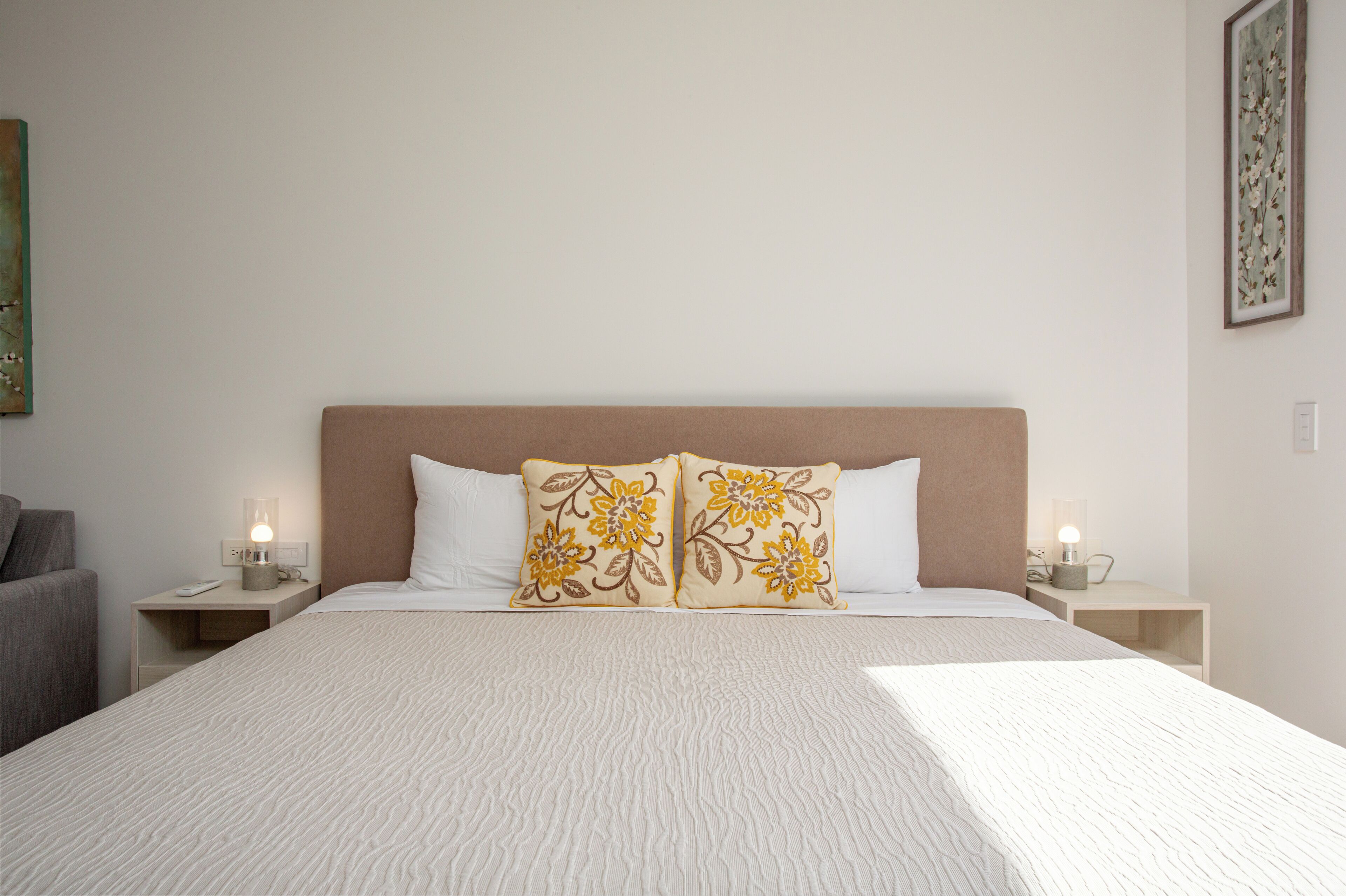 A neatly made bed with a textured white cover, two decorative pillows with floral patterns, and bedside lamps on either side.