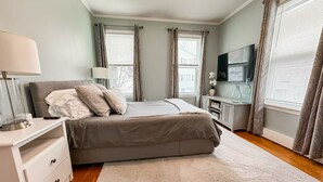 A bedroom with a bed, bedside tables, a TV, and curtains. - Southie Condo - Near Subway - Bring Pets - Pool Table (Boston)
