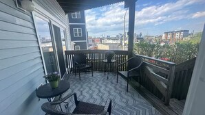 A covered balcony with a patterned floor, two chairs, a small table, and a potted plant. - Southie Condo - Near Subway - Bring Pets - Pool Table (Boston)