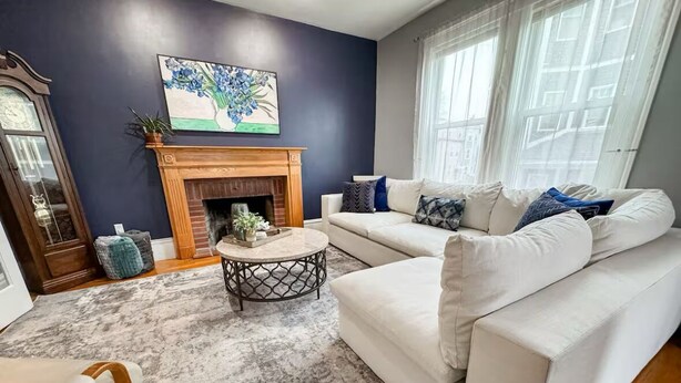 A living room with a fireplace, white sofas, a coffee table, and a large painting on the wall. - Southie Condo - Near Subway - Bring Pets - Pool Table (Boston)