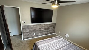 A bedroom with a bed, a ceiling fan, a mounted TV, and a door leading to another room. - Newly remodeled 3-bedroom ranch with pool table, patio, and grill in Urbandale. (Urbandale)