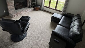 A living room with a fireplace, a black leather sofa, a recliner, and a television mounted on the wall. - Newly remodeled 3-bedroom ranch with pool table, patio, and grill in Urbandale. (Urbandale)