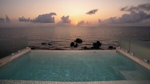 An infinity pool with a clear view of the ocean and sunset.