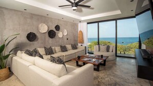 A modern living room with a sofa, coffee table, and a large window offering a view of the ocean.