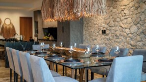 A modern dining area with a stone wall backdrop, a long table set with plates and glasses, and a unique woven light fixture above.