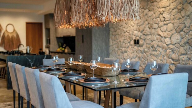 A modern dining area with a stone wall backdrop, a long table set with plates and glasses, and a unique woven light fixture above. - Casa Serena: Oasis in front of the Caribbean with Pool and Terrace (Isla Mujeres)