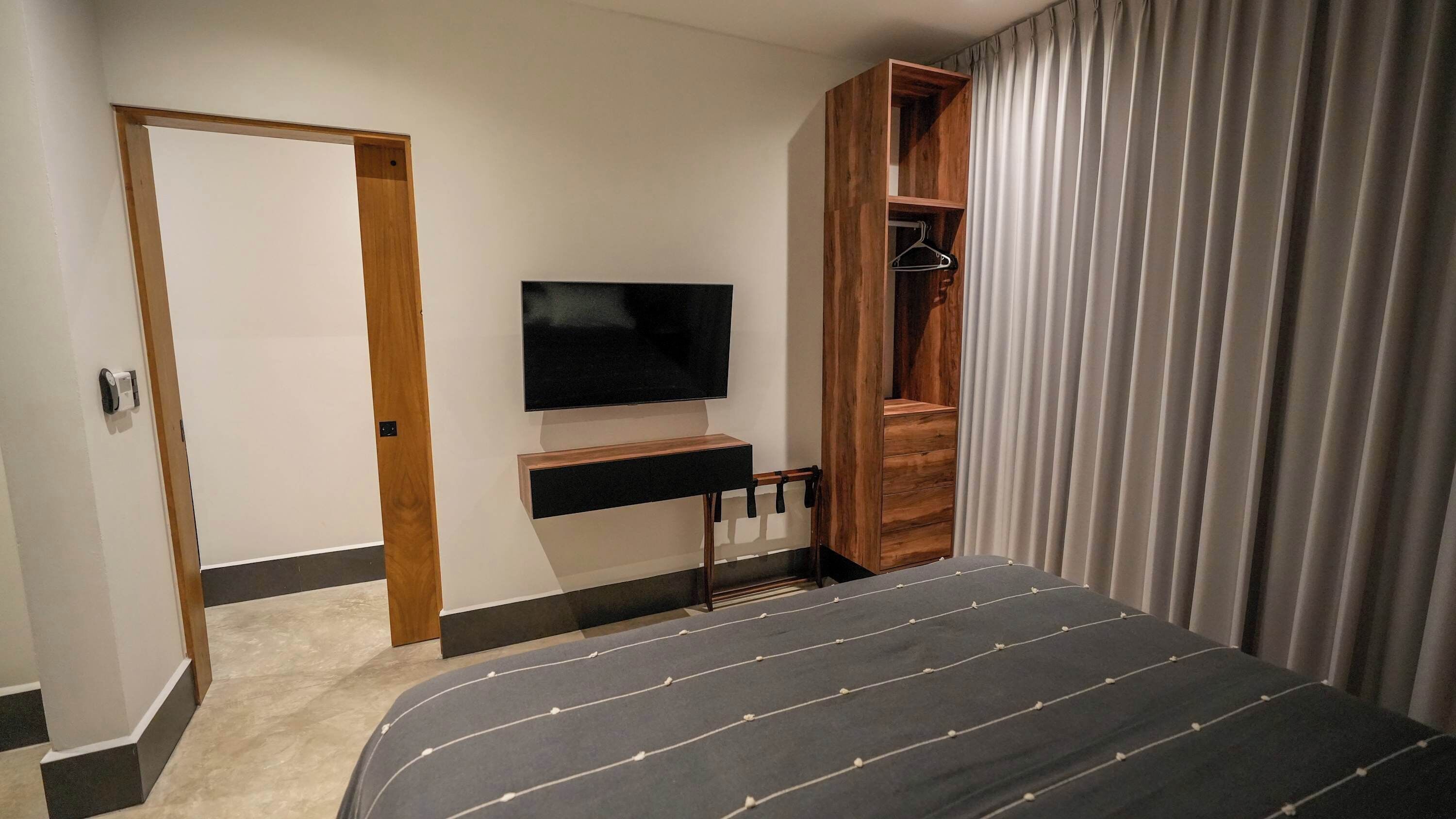 A hotel room with a bed, a TV, a wooden wardrobe, and a door.