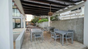 Une terrasse extérieure couverte, dotée de tables et de chaises, une piscine et un mur en pierre.
